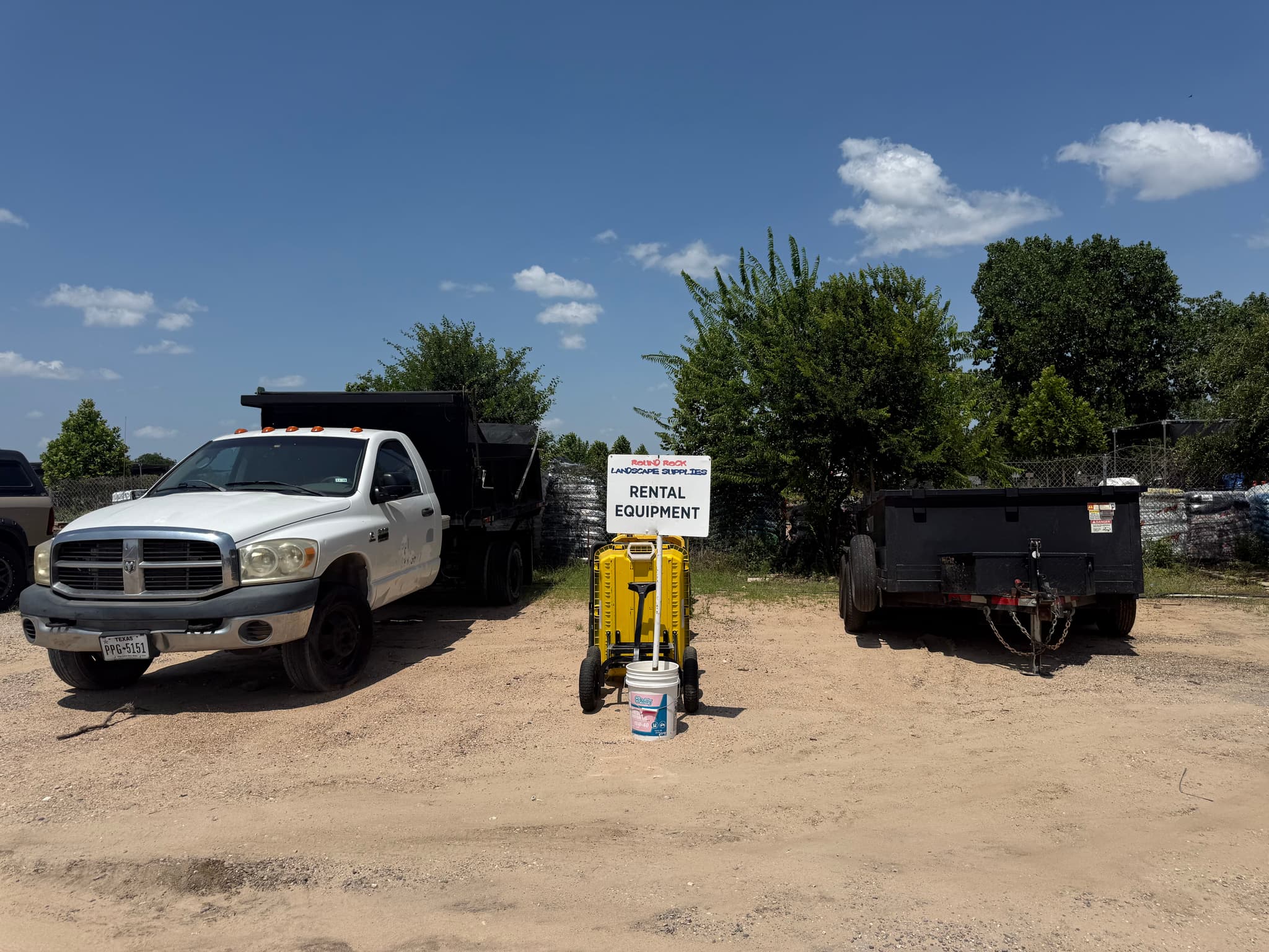 Rental equipment sign beside a hauling cart, dump truck and trailer at the Round Rock Landscape Supplies™ yard
