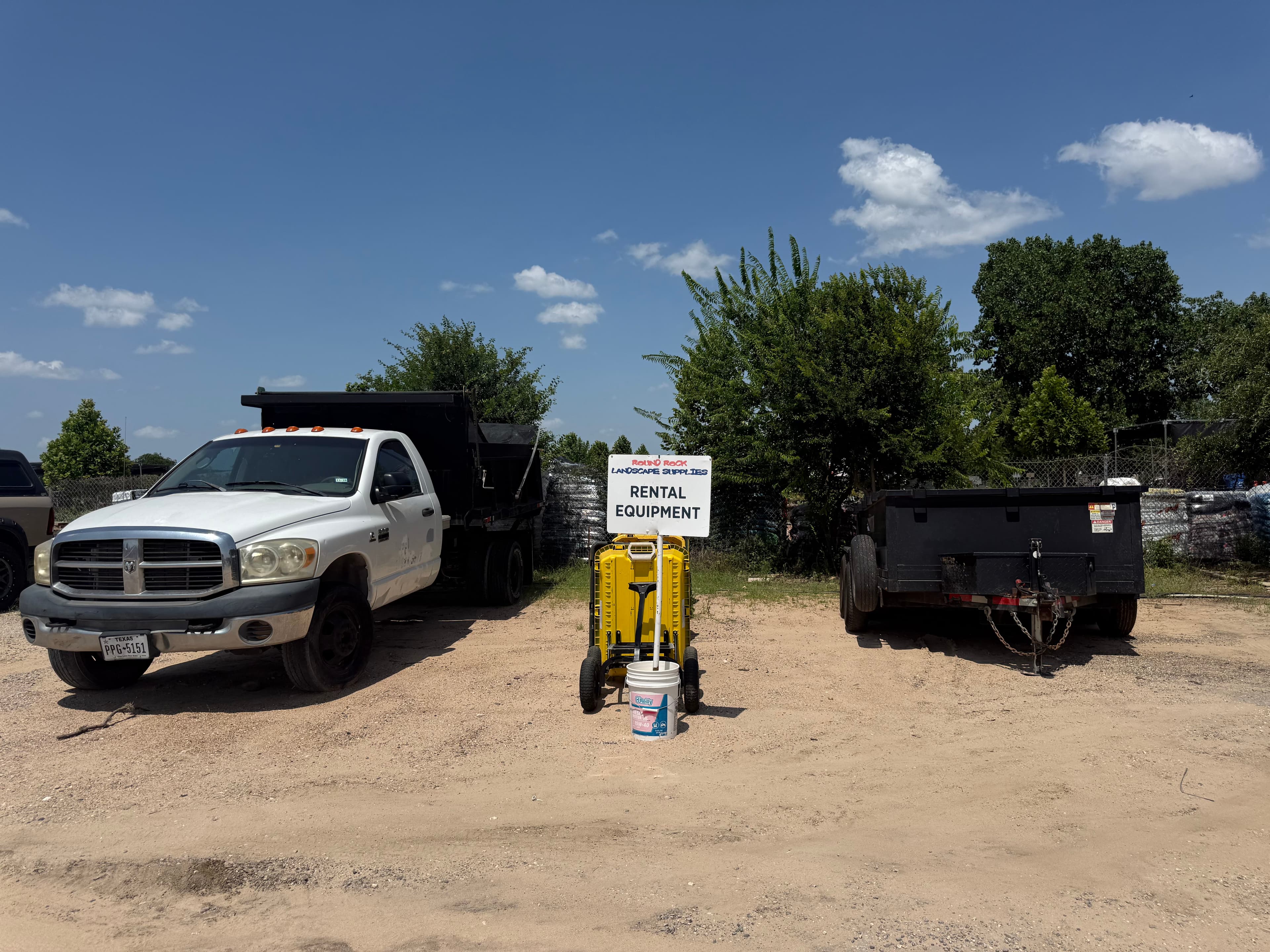 Rental equipment sign beside a hauling cart, dump truck and trailer at the Round Rock Landscape Supplies yard
