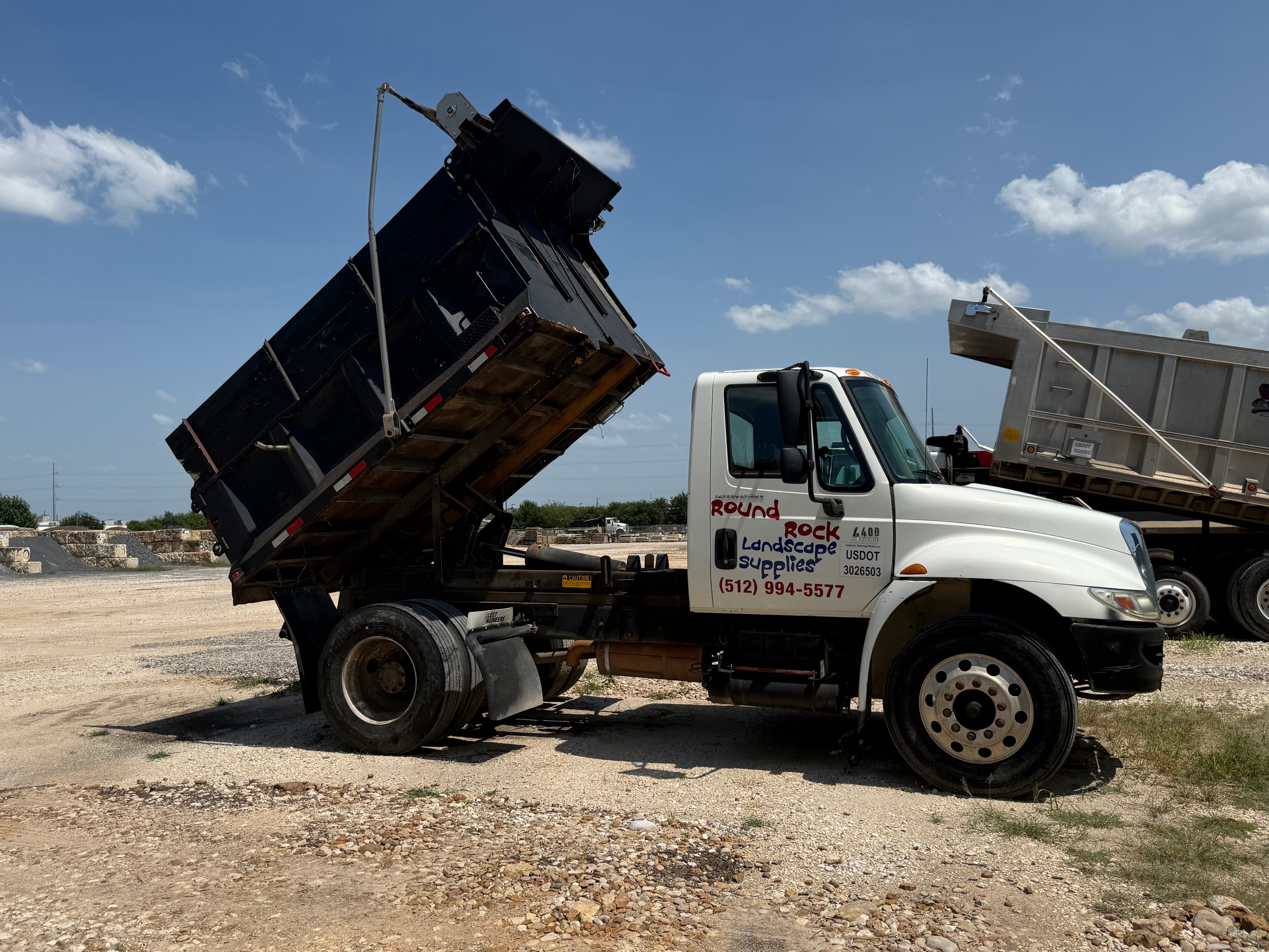 Round Rock Landscape Supplies branded dump truck with its bed raised, ready to haul bulk material